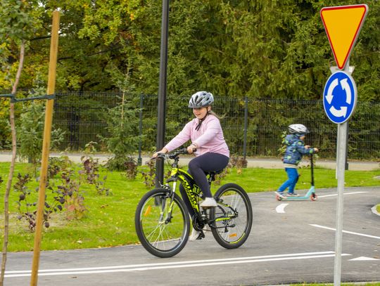 Dziewczynka w kasku jeżdżąca na rowerze po miasteczku ruchu drogowego w pobliżu znaku ustąp pierwszeństwa i ruchu okrężnego