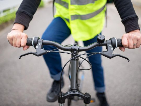 Rowerzysta w kamizelce odblaskowej trzyma kierownicę na ulicy, podkreślając bezpieczeństwo na drodze.
