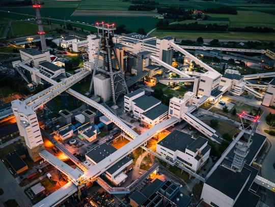 Widok z lotu ptaka na przemysłowy kompleks kopalni węgla kamiennego LW Bogdanka, z widocznymi wieżami szybowymi i systemem taśmociągów, oświetlony w godzinach wieczornych.