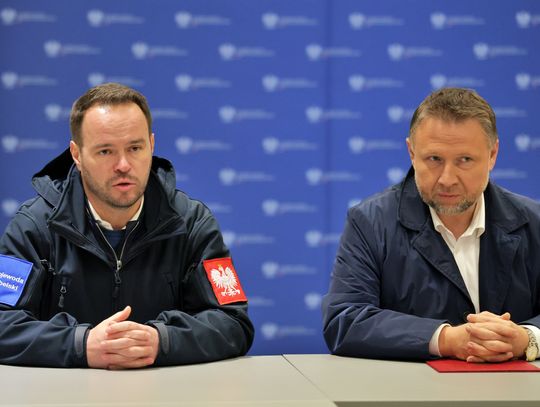 Wojewoda lubelski Krzysztof Komorski (po lewej) oraz minister spraw wewnętrznych i administracji Marcin Kierwiński (po prawej) siedzą przy stole podczas ogłaszania Programu OLiOC dla województwa lubelskiego. Wojewoda ma na kurtce naszywki "Wojewoda Lubelski" i godło Polski.