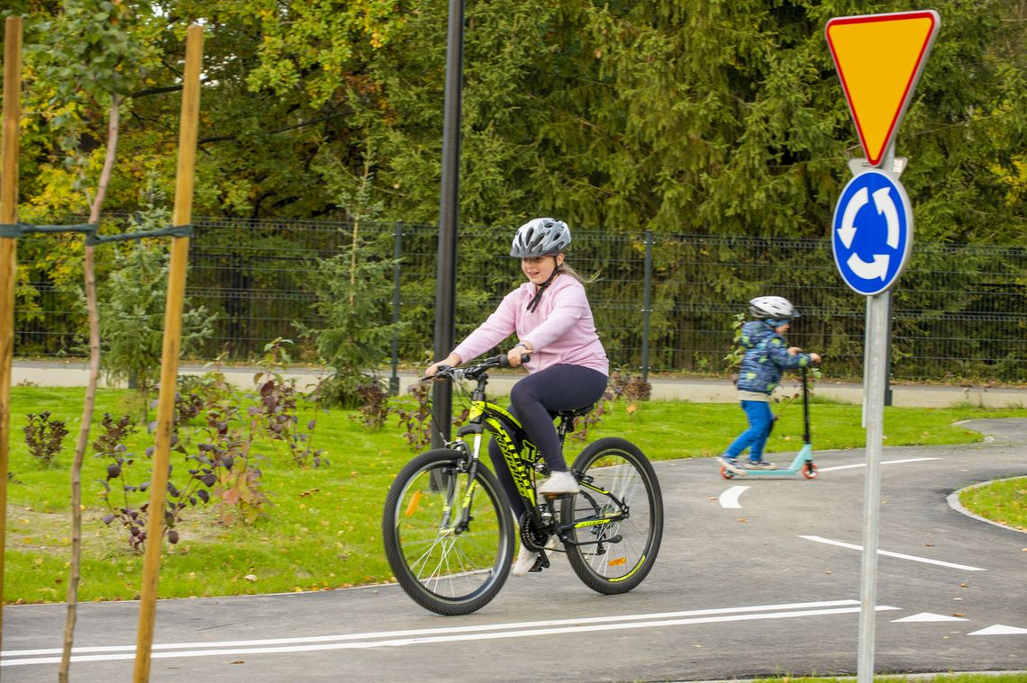 Duże zmiany dla młodych rowerzystów. Karta rowerowa już od 9. roku życia Dziewczynka w kasku jeżdżąca na rowerze po miasteczku ruchu drogowego w pobliżu znaku ustąp pierwszeństwa i ruchu okrężnego
