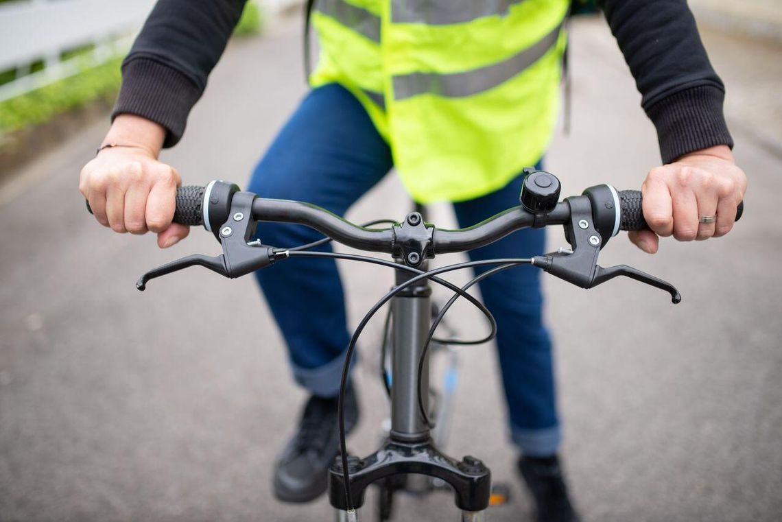 Jesienny zmrok i brak widoczności. Dlaczego elementy odblaskowe ratują życie? Rowerzysta w kamizelce odblaskowej trzyma kierownicę na ulicy, podkreślając bezpieczeństwo na drodze.