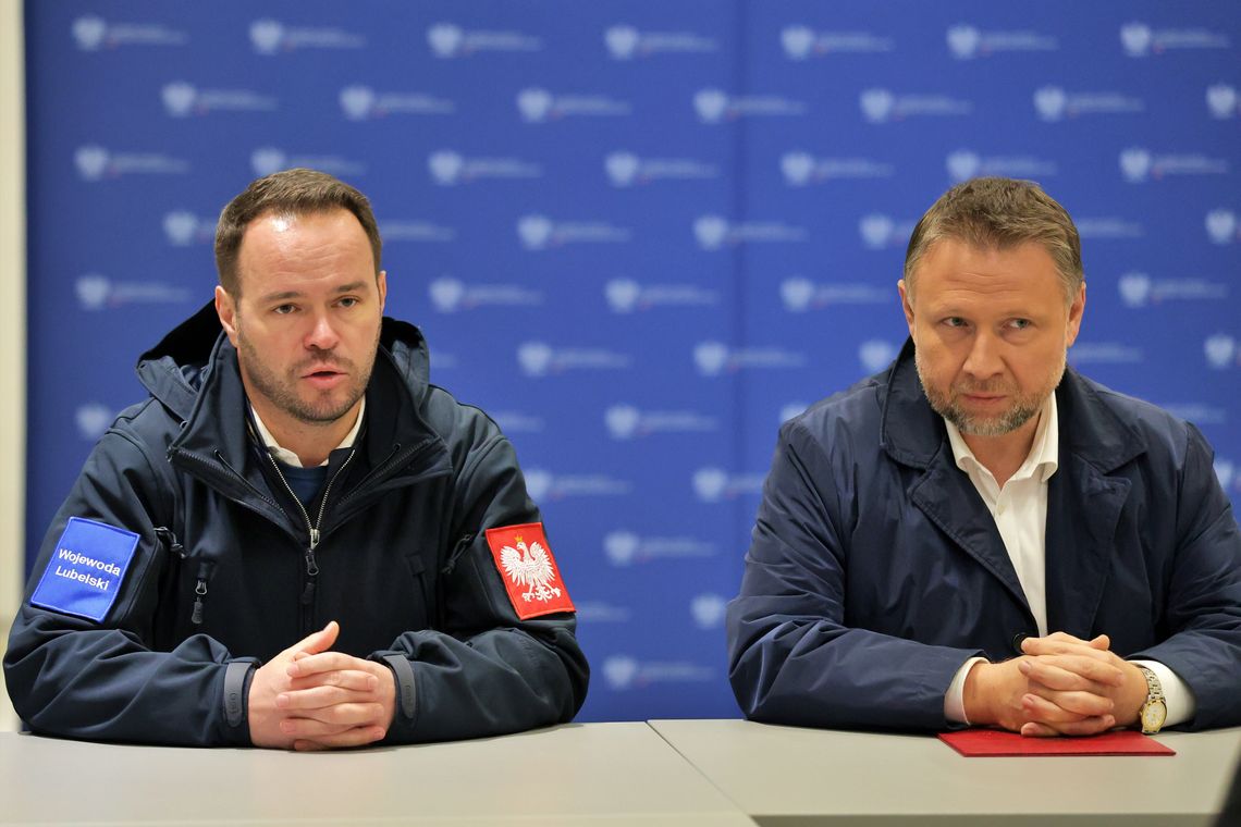 Wojewoda lubelski Krzysztof Komorski (po lewej) oraz minister spraw wewnętrznych i administracji Marcin Kierwiński (po prawej) siedzą przy stole podczas ogłaszania Programu OLiOC dla województwa lubelskiego. Wojewoda ma na kurtce naszywki "Wojewoda Lubelski" i godło Polski.